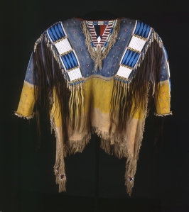 Chemise cérémonielle ayant appartenu au chef Red Cloud, Oglada Lakota. Ces chemises, portées lors de grandes occasions, étaient l’attribut des hommes importants. Brodée de bandes de perles de verres, elle est ornée de cheveux humains (soit des scalps pris à l’ennemi, soit des mèches offertes par les membres de la famille du guerrier), le bleu symbolise le ciel et le jaune la terre. La partie centrale indiquait la position sociale du porteur. Chez les Sioux, ils étaient six ou sept par tribu : un chef de guerre, un gestionnaire des problèmes internes, un chargé des relations avec les Européens… © Buffalo Bill Center of the West, Cody, Wyoming, USA, Adolf Spohr Collection, don de Larry Sheerin. Inv. NA.202.598.