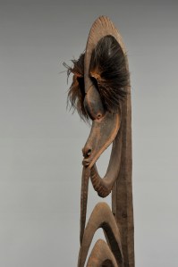 Charme de chasse anthropomorphe (détail), Alamblak, rivière Karawari, cours moyen du fleuve Sepik. Dénommés yipwon, ils étaient invoqués dans la préparation des expéditions guerrières. Chaque homme en possédait plusieurs, hérités de ses ancêtres ou sculptés par lui-même. De différentes tailles, ces figures sont toujours composées d’une large tête surmontant un corps squelettique et, parfois, d’un pied. L’arc sommital évoquerait une coiffure et l’arc sous le menton un bras. Le corps se compose d’une série de crochets représentant les côtes du personnage. Ces sculptures représentent des ancêtres mythiques qui étaient associés à la chasse et à la guerre. Les exemplaires de grande taille étaient la propriété d’un groupe familial ou d’un clan. Conservées dans la maison des hommes, seuls les initiés pouvaient les contempler. Avant de partir à la chasse ou à la guerre, elles étaient activées par une offrande de nourriture ou enduites d’une substance à laquelle était attribuée un pouvoir particulier. Bois, plumes de casoar et pigments. H. : 189,2 cm. Acquis par voie d’échange avant 1970. © MRAC. Inv. EO.1970.89.4.