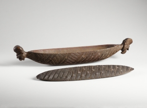 Boîte à plumes, Maori, côte est de l’île nord (baie de Plenty), Nouvelle-Zélande (objet non exposé). Milieu du XIXe siècle. Chaque extrémité est ornée d’un visage expressif sculpté en ronde bosse. Les côtés et le couvercle sont couverts d’un motif d’entrelacs et de petites lignes transversales. Les pendentifs de jade et les plumes de l’oiseau « huia », dont les Maori se servaient pour orner leurs manteaux, étaient conservés dans ces boîtes. Ces coffrets pouvaient être suspendus aux chevrons de la case par les excroissances sculptées à leurs extrémités. La forme oblongue rappelle celle des pirogues et renvoie aux mythes d’arrivée des premiers clans maoris par pirogue. Bois. L. : 56. © Musée du quai Branly, 71.1885.52.96.1-2. Photo : Claude Germain.