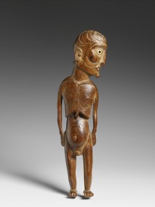 Statuette masculine moai kavakava, Rapa Nui (île de Pâques), Polynésie de l’Est, milieu du XIXe siècle (objet non exposé). La tête, dont le crâne est gravé de motifs en croissant, est tournée sur le côté. Les yeux sont incrustés de coquillage et la pupille gauche conserve encore un disque d’obsidienne. En pascuan, le terme « moai » désigne toute sculpture humaine ou animale tandis que « kavakava » renvoie aux esprits des morts et des ancêtres. Les côtes saillantes et les traits émaciés du visage, caractéristiques de ce type de représentation, évoquent ainsi le monde de l’au-delà. Certaines de ces figures pouvaient être portées autour du cou. D’autres étaient manipulées lors de rituels. Transmises de génération en génération, toutes étaient précieusement conservées dans les maisons, enveloppées dans de l’étoffe d’écorce. La forme générale et la représentation de profil suivent les formes tortueuses du morceau de bois. Bois de Sophora toromiro, coquillage et obsidienne. H. : 29,3 cm. Inv. : 72.53.290. © Musée du quai Branly. Photo Patrick Gries.