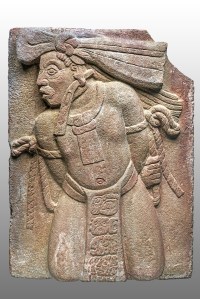 Haut-relief en grès montrant un captif, la bande de toile ou de papier pendue à son oreille indique son sacrifice imminent. Son pagne porte l’inscription de son nom et de son origine, ainsi que celui de son vainqueur. Début du VIIIe siècle. Classique récent (600-800 ap. J.-C.). Monument 154 de Toniná, Chiapas, Mexique. © Museo Nacional de Antropología, Mexico. Photo : I. Guevara. Réf. : Maya-NCH-3090.