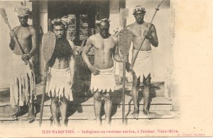« Îles Marquises. — Indigènes en costume ancien, à Taiohae, Nuka-Hiva. A. Itchner, Huahine. ». 8,8 x 13,7 cm. Au centre les deux personnages sont coiffés d’une couronne hei kohio ou peue’ei ou peue’koi’o et tiennent des pagaies hoe. Celui de gauche porte un casque en peau de poisson porc-épic (Diodon holocanthus) tel qu’on en trouvait aux îles Gilbert (Kiribati) tandis que celui de droite est orné d’une couronne paekaha, et tiennent des massues u’u.